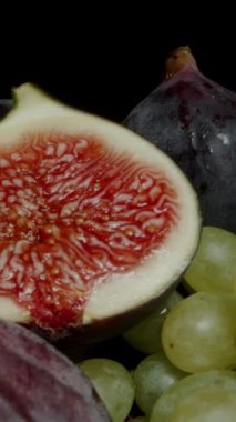 Dikey video. Dilimlenmiş incir yarılarını siyah ve yeşil üzümlerin üstüne yerleştirdim. Dolly kaydırıcı aşırı yakın çekim.