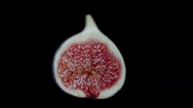 Yarım olgun ve sulu incirli kırmızı hamurlu, siyah arka planda dönen. Kesmek için izole edilmiş.