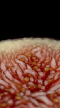 Dikey video. Kırmızı ve sulu hamurlu bir incirin yarısı Kara Arkaplan 'da döner ve kamera yukarıdan geriye doğru hareket eder. Kaydırıcı, Makro.