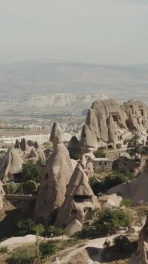 Dikey video. Türkiye 'deki antik bir kentin vadisinin yukarısından gelen panorama, evlerin doğrudan büyük yüksek kayalara oyulduğu yer..