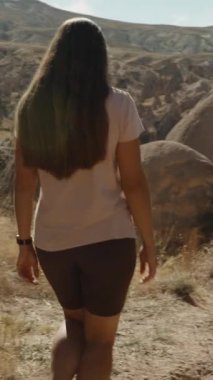 Dikey video. Genç kadın kadim büyük taşlarla kavurucu güneşin altında çorak bir vadide seyahat ediyor..