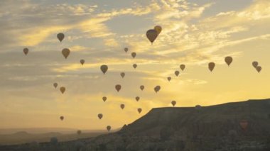 Güneş doğarken sıcak hava balonları olan vadi, dağların arasından yükselen güneş bulutları altın rengine boyadı, Kapadokya, Türkiye.