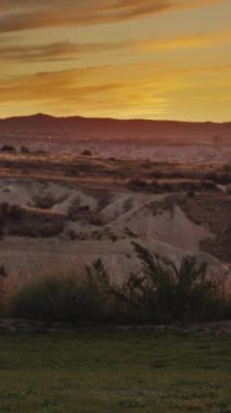 Dikey video. Genç bir kadın gün batımının tadını çıkarmaya geldi. Çimlerin üzerine bir yastık koydu ve oturdu, önünde dağ manzarası ve kanyon ile.
