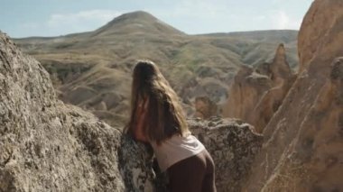 Antik taştan bir vadide, uzun bir dağa bakan genç bir kadının manzarası..