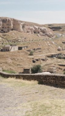 Dikey video. Türkiye 'nin Saratli antik kentinde tepelerin eteklerindeki evleri gören genç bir kadın yürüyor.