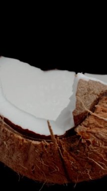Dikey video. Çatlak bir hindistan cevizinin yarısı, izole edilmiş siyah arka planda döngülenmiş video..