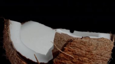 Kırık bir hindistan cevizine yakın plan, beyaz et, siyah arka plan üzerinde dönüyor..