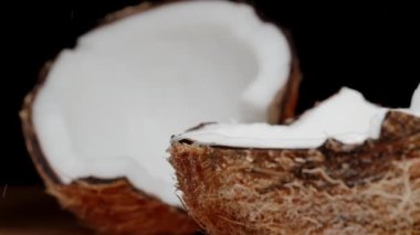 İki parçaya ayrılmış kırık bir hindistan cevizi, tepesinden damlayan bir damla meyve suyu. Yakın çekim, yavaş çekim..