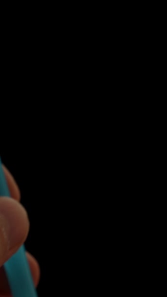 バーティカルビデオ クローズアップの男の手は黒い背景にココナッツに青いわらを挿入する — ストック動画
