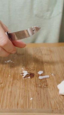 Dikey video. Bir kadın tabaktan hindistan cevizi parçaları alıyor ve özel bir bıçakla derilerini yüzüyor. Kaydırıcı onu yakın planda yakalar.