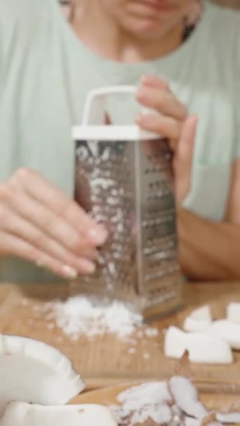 バーティカルビデオ キッチンにいる若い女性は ココナッツを金属製のグレーターを使用して数百人に与え 偶然彼女の指を切ります — ストック動画