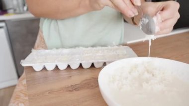 Kadın, hindistan cevizi parçalarını plastik kalıba koyar, sütü sıkarak şeker yapar..