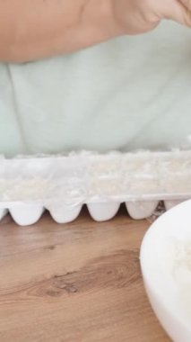 Dikey video. Kadın, hindistan cevizi parçalarını plastik kalıba koyar, sütü sıkarak şeker yapar..