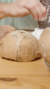 Dikey video. Hindistan cevizi parçaları ve beyaz et parçaları masaya yayılmış, ve arka planda, kadın şeker için hindistan cevizi talaşı yapmak için onları rendeliyor, yavaş çekimde..
