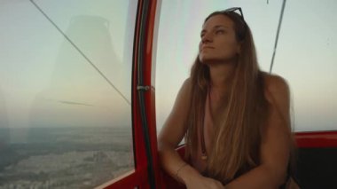 Gezgin genç bir kadın dağlarda bir teleferik kulübesinde oturuyor, gün batımını seyrediyor ve olumlu bir şeyler düşünüyor..