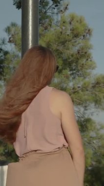 Dikey video. Genç bir kadın ağaçların arasından geçen bir yükseklikten denize hayran, Rüzgarda uçuşan uzun saçları.