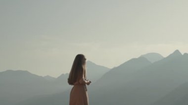 Batan güneşin yumuşak sinematik ışığında dağların ortasında genç bir kadın etrafına bakar ve manzaralardan büyülenir. Seyahatte yeni bir hayat kavramı.