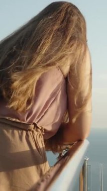 Dikey video. Genç kadın korkuluklara eğilip tepeden aşağı bakarken deniz ve dağların nefes kesici manzarası. Dağların zirvesinde özgürlük ve hafiflik.