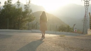 Yüksek Topuklu Genç Kadın, bir asfalt yolda dağdan Sunset 'e doğru iniyor. Yavaş Çekim, Sinematik Aydınlatma.