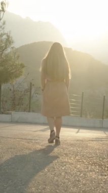 Dikey video. Yüksek Topuklu Genç Kadın, bir asfalt yolda dağdan Sunset 'e doğru iniyor. Yavaş Çekim, Sinematik Aydınlatma.
