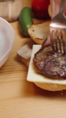 Dikey video. Peynirin ve kırmızı sosun çoktan yerleştirildiği bir çöreğin üzerinde hamburger için köfte yapan bir kadın..