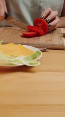 Dikey video. Ev Hayatı ve Yemek Hazırlama, bir kadın domatesleri dilimler ve kamera daha da yakınlaşır. Ev yapımı burgerler.