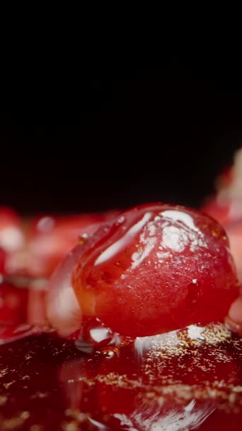 垂直录像 在黑色的背景上 红色的石榴种子 上面滴着果汁 慢慢地从种子上级联 后续行动 — 图库视频影像