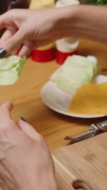 Dikey video. Hamburgerdeki Domatesin Üzerine Bir Kadın Marul Yapıyor. Sıcak, ev atmosferi ve kendini hazırlayan yiyecek..