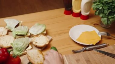 Bir kadın ev yapımı hamburgerler yapıyor, içindekiler masaya serilmiş. Bir salatalık alır, arkadan seyreder. Yavaş Çekimde.