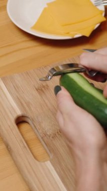 Dikey video. Ev Hayatı ve Elle Hamburger Yapımı. İnce Şeritlere Salatalık Kesen Bir Kadının Arkasından Görüntü.