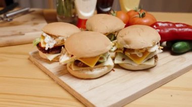 Tahta Masa 'da ev yapımı hamburgerler, yanında da sos şişeleri var. Sinematik ışıklandırma ve kamera hareketleri.