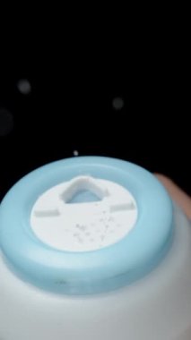 Dikey video. Şef plastik tuzluktan tabağı tuzlar ve küçük tuz tanecikleri yavaşça düşer. Siyah bir arkaplanda, yakın plan.