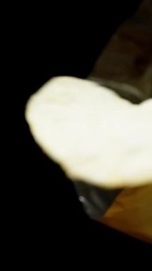 Dikey video. Patates cipsi paketin tepesinden düşer. Onları bir tabağa dolduracağım ve televizyon izlerken rahatlayacağız. Yavaş çekim makrosu.
