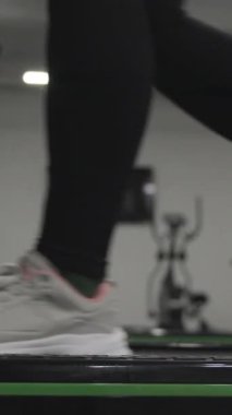 Dikey video. Spor salonunda bir kadın yavaşça koşu bandında yürüyor. Hareket halindeki Atletik Yaşam.