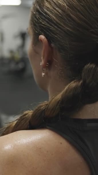垂直录像 从一个年轻女子坐在镜子前的固定自行车上练习的后面看 她的背已经汗流浃背了 — 图库视频影像