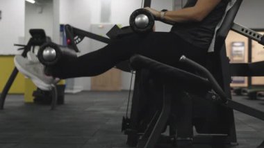 Oturan bir makinede bacak egzersizi yapan genç bir kadın..