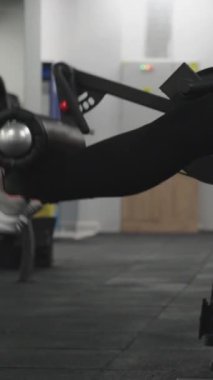Dikey video. Oturan bir makinede bacak egzersizi yapan genç bir kadın..