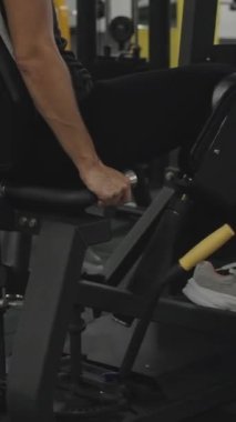 Dikey video. Spor Salonunda Siyah Pantolon Giyen Kadın Spor Makinesinde Bacak Kaçırma Yapıyor. Arka Görünüm!