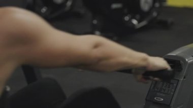 Ağır çekimde kürek çekme makinesinde egzersiz yapan terli dişinin arkasından bakın. Yakın plan..