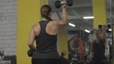 Her iki koluyla da Kıvırcık Kıvırcık 'ı oynayan genç bir kadın. Terli Sırt Parıltısı, Arkadan Görüntü. Salondaki Aynanın Önünde!