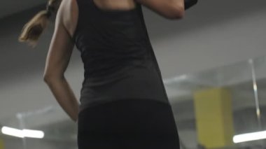 Spor salonundaki genç kadın çok ağır bir dambılı tutuyor. Onu kaldırıyor ama yukarı itmek için çabalıyor. Antrenmanın sonunda yorgun ve zayıf düştü..