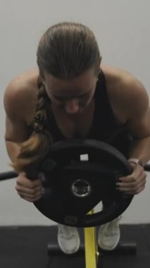 Dikey video. Sırtın gelişmesi için egzersiz. Genç bir kadın spor salonunda ekstra ağırlıkla hiperuzatma egzersizi yapıyor..