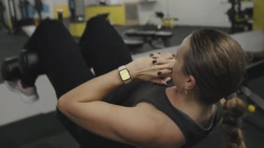Uzun saçlı at kuyruklu genç bir kadın spor salonundaki eğimli bir bankta karın egzersizi yapıyor..