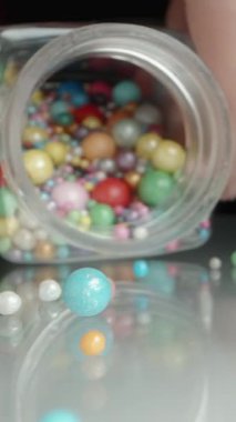 Dikey video. Küçük Kavanozdan, Dekorasyon İçin Farklı Boyutlarda Tatlı, Çok Renkli Toplar Döküyorum. Kameraya doğru ağır çekimde Makro çekimde ilerliyorlar..