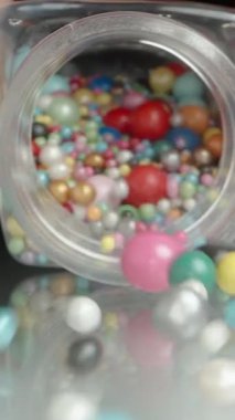 Dikey video. Çok renkli jöleli şeker topları, şekerleme serpintisi, kavanozdan masaya saçılan şeker. Yavaş Hareket, Yakın Çekim.