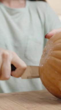 Dikey video. Bir kadın küçük bir balkabağını ikiye böldü. Tahta Masa 'ya yakın çekim.