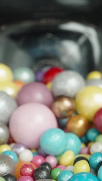 バーティカルビデオ シュガーボールとジャー 多色の釉薬 内部からの眺め 黒い背景に対してテーブルの上に散らばったボール ドリースライダー極端なクローズアップ — ストック動画