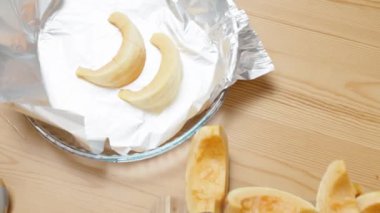 Kadın küçük balkabağı parçalarını soyar, derisini yüzer ve onları folyo kaplı bir çarşafa koyar..