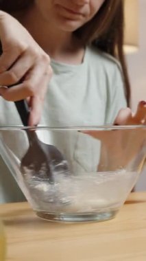 Dikey video. Genç kadın kasede beyaz karışımı karıştırıyor. Yemek pişiriyor.