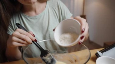 Genç bir kadın kurabiye hamuru hazırlarken hamura hindistan cevizi gevreği ekler. Ağır çekimde.